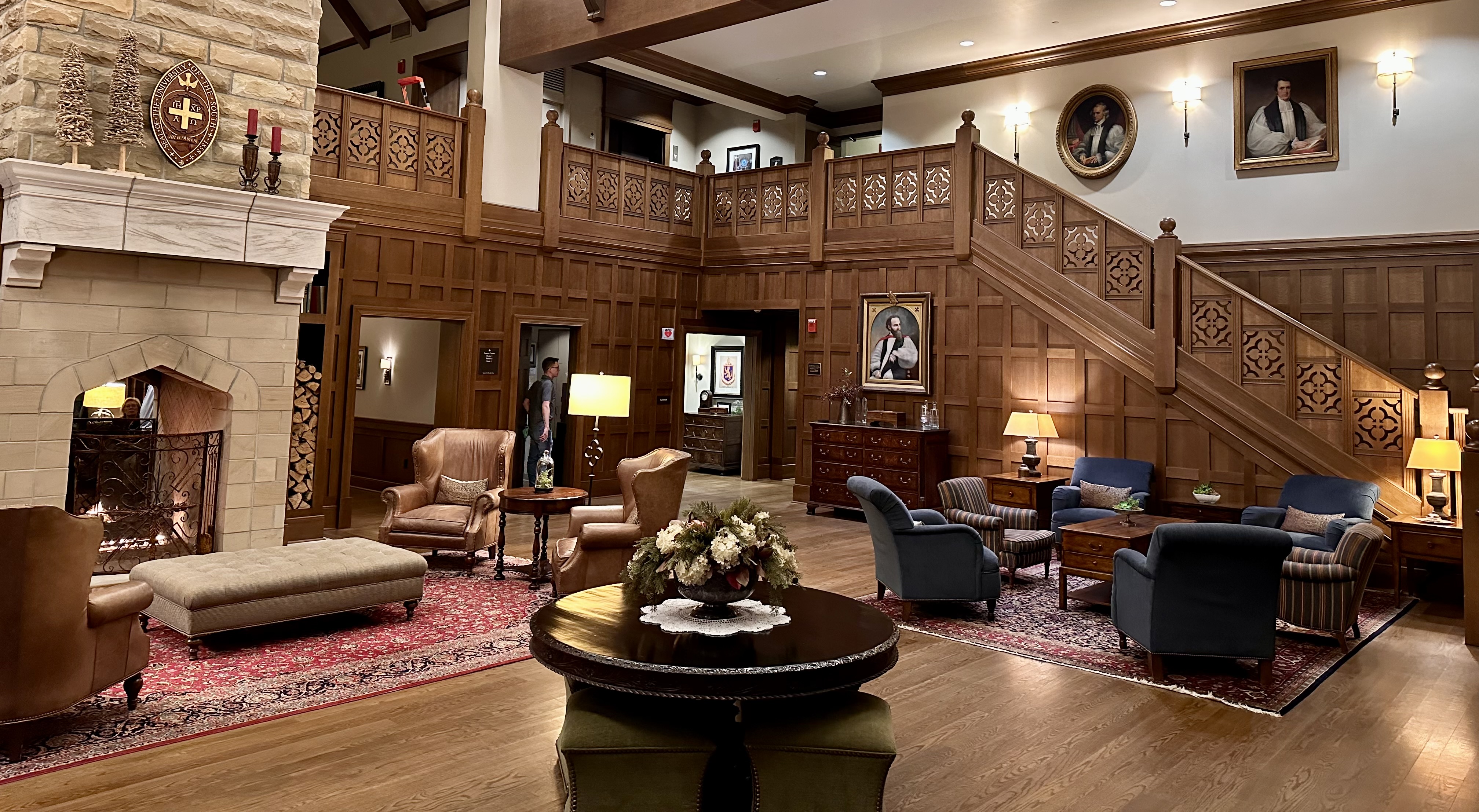 A photo of the lobby of the Sewanee Inn, with stone fireplace, paneled stairway, and portraits of Sewanee clergymen.